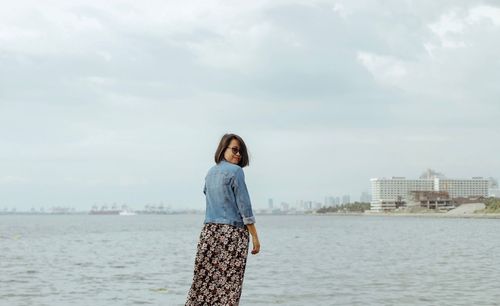 Young woman standing at beach against sky