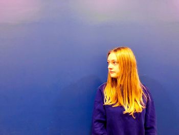 Young woman standing against blue wall