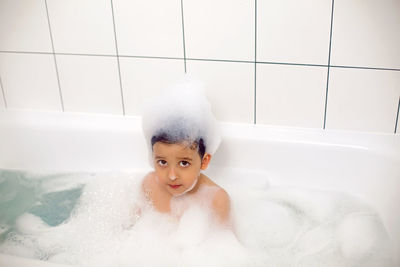 Boy with big eyes a caucasian child bathes in a white bath with foam