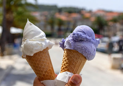 Personal perspective of hand holding two ice cream cones with lavender and lemon flavour