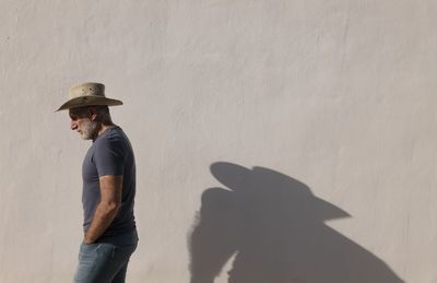 Portrait of adult man in cowboy hat against white wall with sunlight and shadow