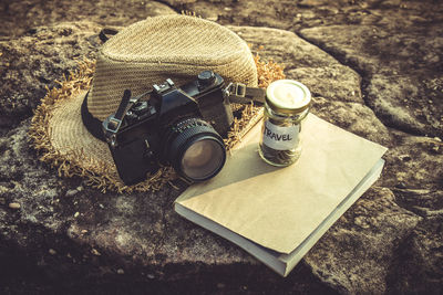 High angle view of dslr camera by straw hat and coins in jar on book