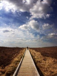 Road passing through field against cloudy sky