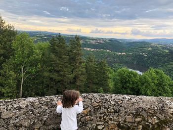 Rear view of girl standing by retaining wall against landscape