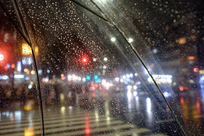 View of illuminated street at night seen through wet glass window