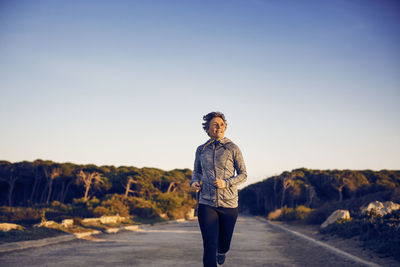 Front view of woman running on road against clear sky