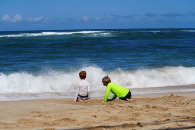 Young boys watching the waves and playing in the sand on the beach in hawaii. 