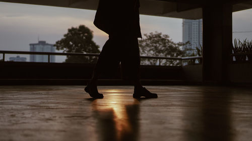 Low section of woman standing on hardwood floor against sun