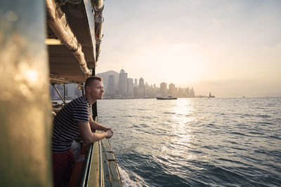 Man standing on boat in city at sunset