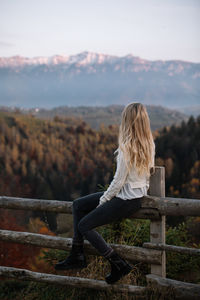 Rear view of woman sitting on railing against sky