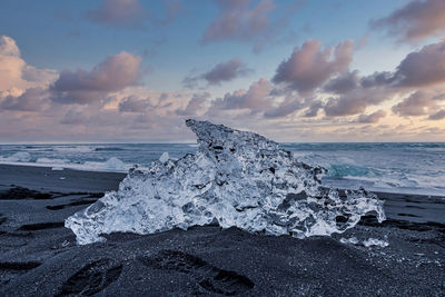 Close-up of iceberg on shore of diamond beach against cloudy sky during sunset