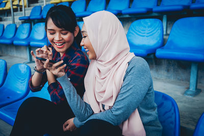 Full length of happy friends sitting on mobile phone