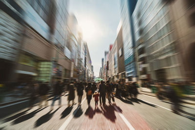 Blurred motion of people walking on street amidst buildings in city