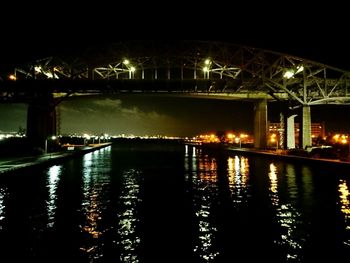 Illuminated bridge over river in city at night