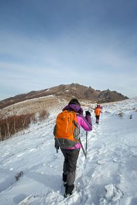 Rear view of hikers climbing mountain against sky during winter