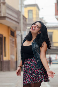 Portrait of cheerful woman standing on footpath in city