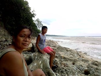 Friends sitting on rock by sea against sky