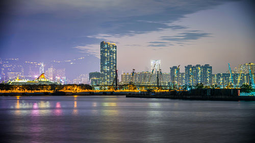 Illuminated city by river against sky