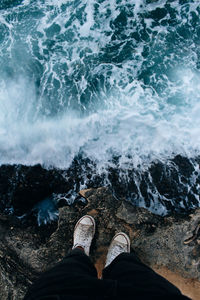 Low section of man standing on rock by sea