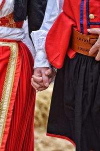 Midsection of couple in traditional clothing holding hands on field