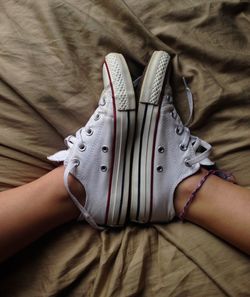 Low section of woman wearing canvas shoes on bed