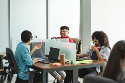 Group of positive hispanic coworkers sitting at table with laptops and communicating while working in modern office in costa rica in daylight