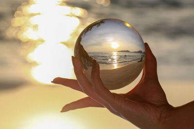 Close-up of hand holding crystal ball against sky