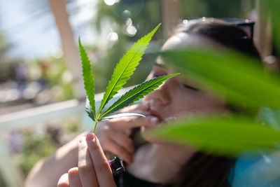 Woman holding cannabis leaves while smoking cigarette
