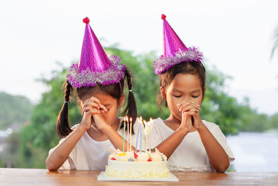 Sisters wishing by birthday cake at home