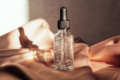 Glass bottle with liquid with bubbles on a pink fabric background. serum or essential aroma oil. 