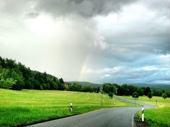 Road passing through grassy field against cloudy sky