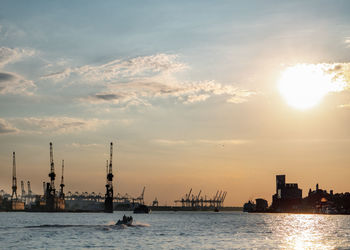 Silhouette city by sea against sky during sunset