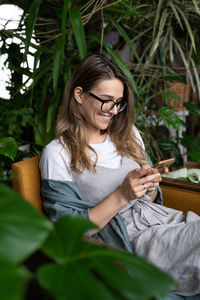 Woman using smart phone while sitting on chair by plants