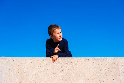 Boy on wall against clear blue sky