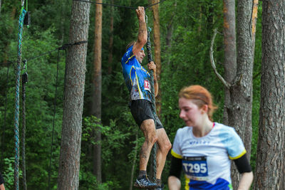 Man and woman standing by tree trunks in forest