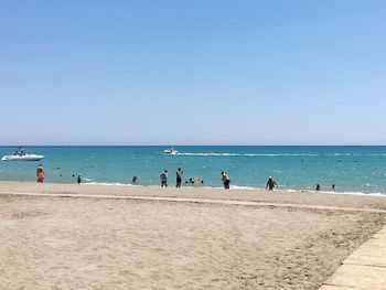 People on beach against clear blue sky