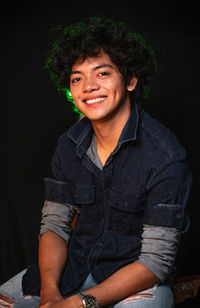 Portrait of smiling young man sitting against black background