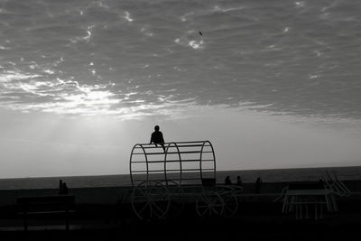 Silhouette man standing by railing against sea during sunset