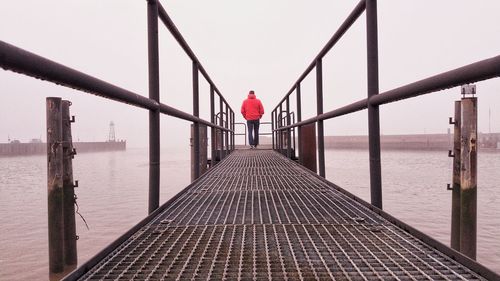 Rear view of man standing on pier by sea against sky