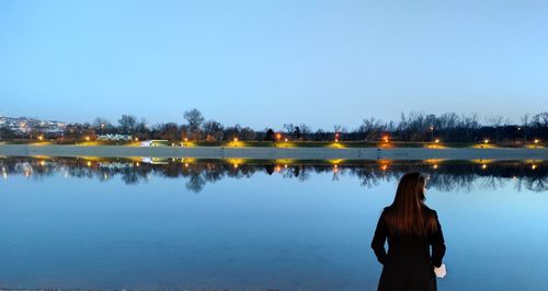 Rear view of woman standing by lake against clear sky