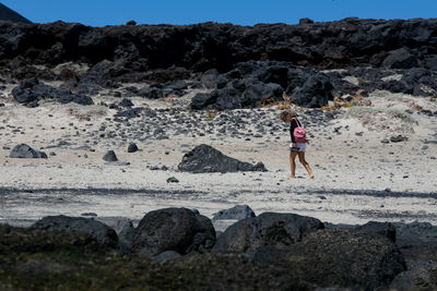 Rear view of woman standing on rock at beach against sky