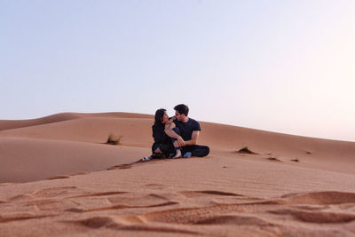 Couple on sand dune in desert against clear sky