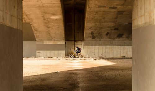 Man riding bicycle on street under bridge