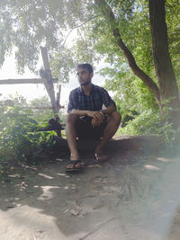 Young man looking away while sitting on tree