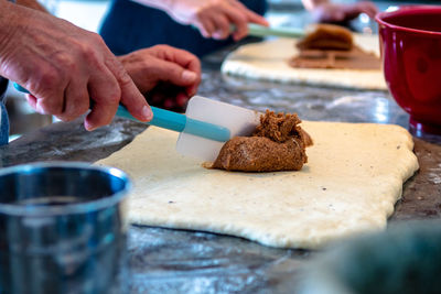 Midsection of bakers making cinnamon rolls in bakery