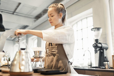 Young female worker preparing coffee at counter