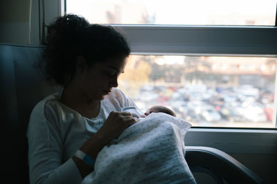 Mother carrying daughter while sitting by window in vehicle