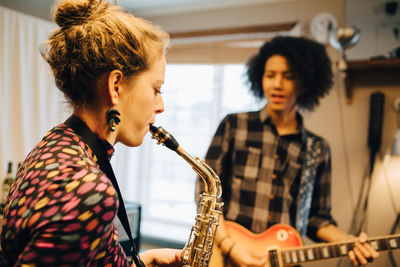 Male and female friends playing saxophone and guitar while practicing at recording studio