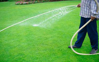Low section of man watering with garden hose at park