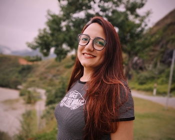 Portrait of smiling young woman standing against trees